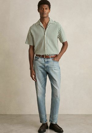 Short-sleeve, button-up shirt with green and white vertical stripes; paired with light blue jeans and dark brown leather shoes.