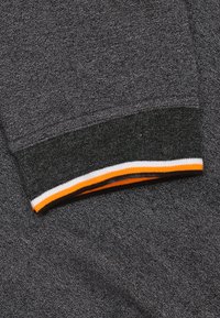 Grijze sweatshirtstof met een gestructureerde afwerking, voorzien van een zwart, wit en oranje gestreepte ribbelboord. Close-up van het mouwdetail.