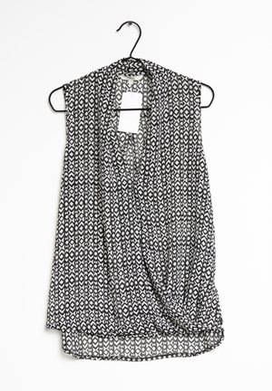 Débardeur sans manches avec un motif géométrique noir et blanc, en tissu léger, au design drapé, et avec un ourlet arrondi, exposé sur un cintre.