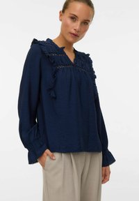 Blusa da donna blu navy con scollatura e maniche a sbuffo, caratterizzata da inserti di pizzo decorativi e una vestibilità comoda. Tessuto testurizzato.