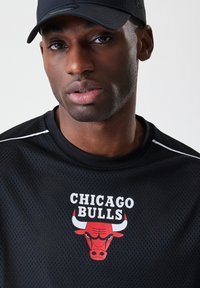 Svart mesh idretts skjorte med teksten "CHICAGO BULLS" og rød bulla logo. Har hvite detaljer på kragen og ermene.