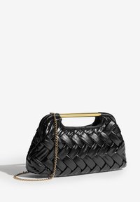 Mustast punutud nahast käekott kuldse kettraami ja ristküliku kujulise kuldse käepidemega, valgel taustal.