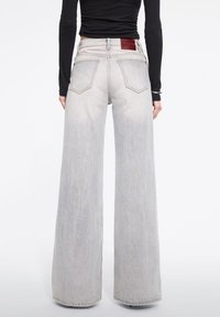 Jeans de pierna ancha de color gris claro con cintura alta, que cuentan con bolsillos traseros y una etiqueta de cuero rojo en la cinturilla. Fabricados en tela de mezclilla.