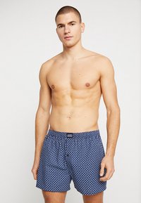 Blå kalsonger med ett vitt prickmönster, elastisk midja och knappgylf, tillverkade av mjukt bomullsmaterial.