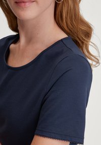 Marineblauwe t-shirt met een ronde halslijn en korte mouwen, voorzien van een textuurstof en gekartelde afwerking langs de randen van de mouwen.