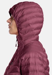 Persona di profilo che indossa una giacca a vento con cappuccio trapuntata color bordeaux, con zip frontale, su uno sfondo chiaro e semplice.