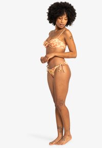 Bikini set v broskyňovej farbe s kvetinovým vzorom, so šnúrkami na nastavenie, bandeau topom s uzlom a bočnými šnúrkami na spodnej časti.