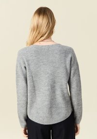 Grauer Strickpullover mit abgerundetem Saum, langen Ärmeln und einer weichen Textur. Verfügt über ein dezentes Rippenmuster entlang der Ränder und des Rückens.