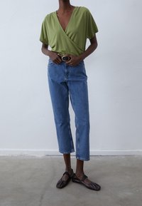 Green wrap top with short sleeves, paired with light blue cropped jeans and black flats, featuring a gold buckle belt.
