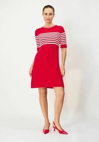 Punainen mekko, jossa on valkoisia vaakaraitoja yläosassa, lyhyet hihat ja suora leikkaus. Yhdistetty punaisiin kärkikengiin.