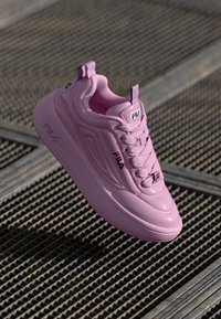 Rosa FILA-Sneaker mit Schnürsenkeln auf einer Metallgitteroberfläche platziert, mit sichtbarem Markenlogo an der Seite, Zunge und Sohle.
