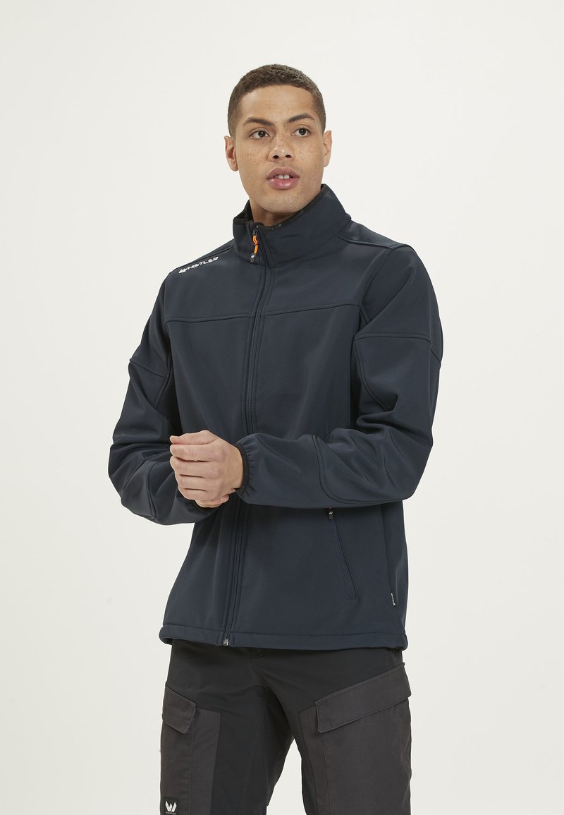 Veste zippée marine avec col montant, poignets élastiques, deux poches zippées et logo sur l'épaule. Tissu lisse et flexible avec une coupe structurée.