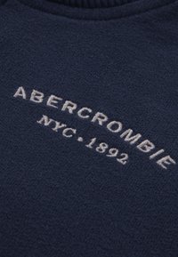 Maglione in pile blu navy con logo ricamato bianco "ABERCROMBIE NYC.1892" sul petto. Tessuto morbido e design a girocollo.