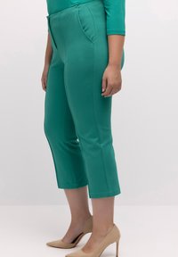 Teal, joustavaa kangasta olevat capri-housut, joissa on etutaskut, puolihyväksyttävä malli ja keskikorkea vyötärö, yhdistettynä nuden värisiin korkokenkiin.