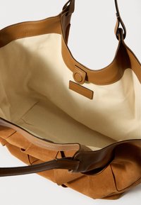 Braune Wildleder- und Leder-Handtasche mit einem weichen, geräumigen Innenraum aus beige Canvas und Druckknopfverschluss. Minimalistisches Design ohne sichtbare Muster.