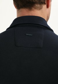 Polo de algodón color navy con un collar texturizado y una pequeña etiqueta negra en la parte posterior con "Garciáno" grabado.