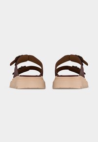 Paire de sandales en cuir marron avec semelles épaisses beiges, dotées de doubles brides avec boucles, vues de dos sur un fond uni.