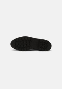 Suela de zapato negra con un patrón de textura en la banda de rodadura; cuenta con ranuras en zigzag para ofrecer agarre y una puntera redondeada. Fabricada en material de goma duradera.