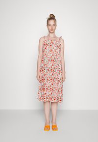 O vestido midi floral apresenta um fundo rosa com flores vermelhas e verdes, alças finas ajustáveis e um design de cintura franzida.