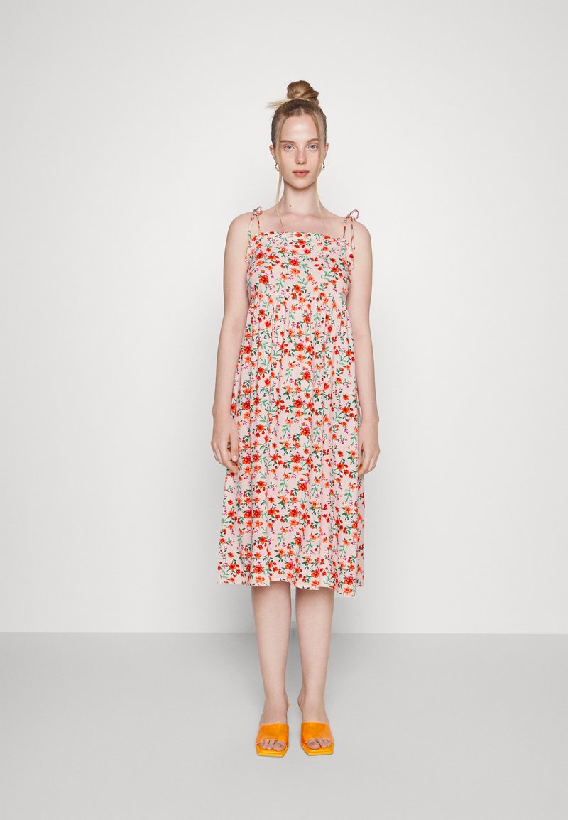 O vestido midi floral apresenta um fundo rosa com flores vermelhas e verdes, alças finas ajustáveis e um design de cintura franzida.