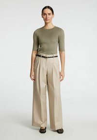 Olivno rebrasto pleteno majico s kratkimi rokavi, v kombinaciji z visokimi bež širokimi hlačami in črnim pasom, dopolnjeno s črnimi tkanimi čevlji.