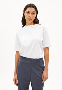 Vit bomullst-shirt med rund halsringning och korta ärmar, kombinerad med byxor i mörkgrått med elastisk midja. Slät textur, minimalistisk design.