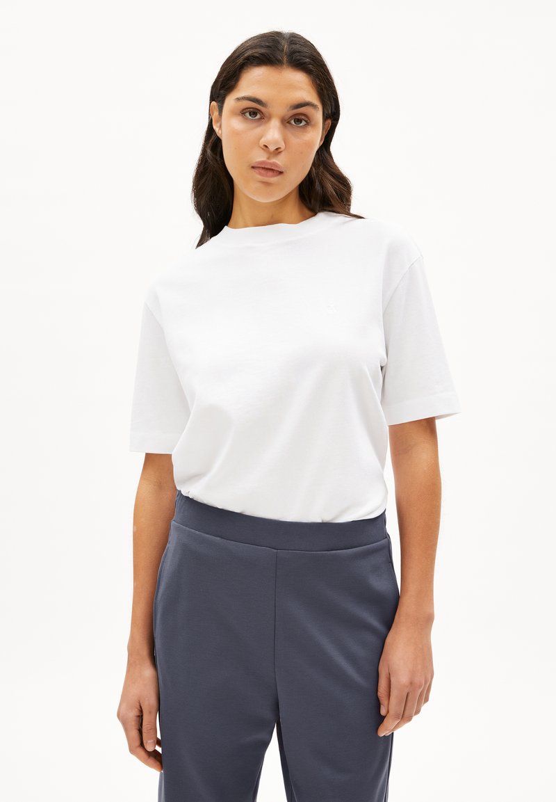 Vit bomullst-shirt med rund halsringning och korta ärmar, kombinerad med byxor i mörkgrått med elastisk midja. Slät textur, minimalistisk design.