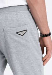 Gray sweatpants featuring a triangular metallic logo patch on the back pocket, with a soft texture and elastic waistband for comfort.