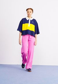 Marineblauw en gele kleurblokkering oversized polo met een witte kraag, gecombineerd met roze wijde broek en donkere sneakers.