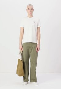Lys grå t-skjorte med korte ermer og et lite grafisk design, sammen med olivengrønne bukser med vid ben og en beigefarget totebag. Hvite sneakers fullfører antrekket.