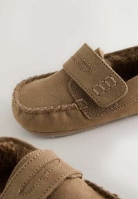 Cezarové semišové slip-on topánky s mäkkou kožušinovou podšívkou, s textúrovaným remienkom a dekoratívnym prešívaním pozdĺž okrajov. Plná gumená podrážka.