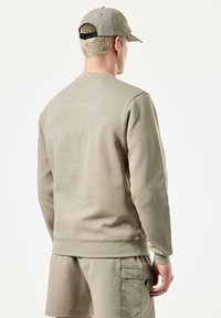 Beige sweatshirt med rund hals, lange ærmer og ribbede manchetter, parret med matchende shorts. Har en tekstureret overflade og minimale sømme.