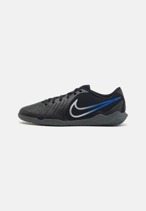 Chaussure de sport noire à profil bas avec fermeture par lacets, semelle texturée et logo Nike bleu et blanc sur le côté.