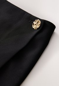 Tessuto nero dalla texture liscia, caratterizzato da un bottone decorativo dorato evidenziato da dettagli intricati sul lato.