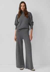Pull en maille gris avec col montant et poignets côtelés, associé à un pantalon gris à jambes larges et taille haute en matière douce et texturée.