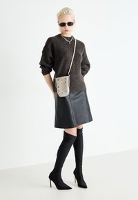 Suéter de punto oscuro, falda de cuero negra, botas ajustadas negras hasta la rodilla y un pequeño bolso cruzado gris con adornos coloridos.