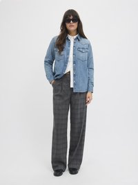 Denimskjorte med trykknapper, to brystlommer; kombinert med grå rutete bukser med vide ben og svarte solbriller. Glatt tekstur, uformell design.