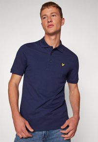 Polo shirt bleu marine en coton, avec un col, une patte de boutonnage à trois boutons et un petit logo d'aigle jaune sur la poitrine.