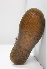 Fialová texturovaná bota s gumovou podrážkou, která má grip s diamantovým vzorem a plochý, zaoblený špičkou. Podrážka je průhledná a má dobře vymezené drážky.