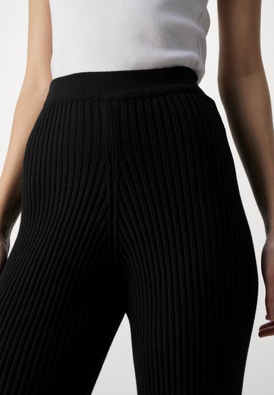 Black ribbed leggings with a high, elastic waistband. The fabric features vertical texture, providing stretch and a snug fit.
