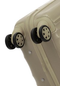Maleta rígida en beige con un exterior texturizado. Cuenta con dos ruedas negras y un cierre, diseñada para la durabilidad y la movilidad.
