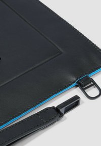 Zwarte leren pouch met blauwe stiksels en hardware, voorzien van een ritsluiting en een afneembare band. Gladde textuur, minimalistisch ontwerp.