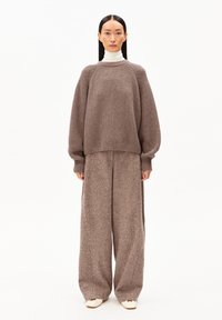 Bruin gestructureerd gebreid sweater met brede mouwen en een cropped zoom, gecombineerd met bijpassende brede broek; beide hebben subtiele details. Crème coltrui eronder.