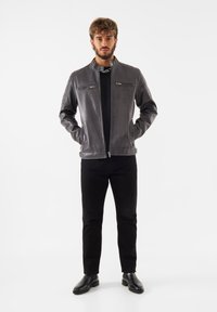 Grå läderjacka med ståkrage, framdragkedjor och axeldetaljer. Kombinerad med svarta byxor och läderskor.