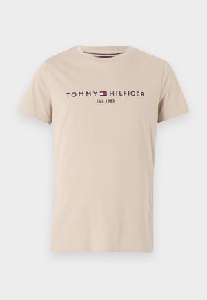 T-shirt in cotone beige con maniche corte, scollatura rotonda, testo blu navy "TOMMY HILFIGER EST. 1985" e piccolo logo a contrasto. Texture liscia.