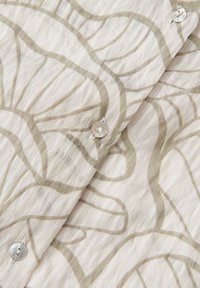 Gros plan d'un tissu beige avec des motifs abstraits en lignes marron clair et des boutons translucides cousus sur un matériau texturé.