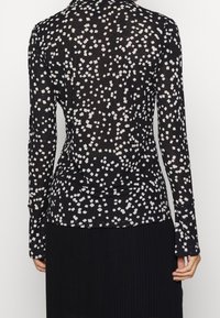 Haut à manches longues noir avec un motif à pois blancs. Tissu fin et doux avec une silhouette ajustée et un col rond.