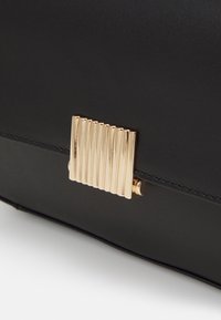 Borsa in pelle nera con una fibbia in metallo dorato rigato, dalla texture liscia e linee pulite, accentuata da cuciture dettagliate.