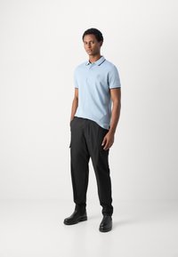 Camisa polo de color azul claro con mangas cortas y un cuello, que presenta un pequeño logotipo. Combinada con pantalones cargo negros y botas negras.