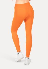 Heldere oranje leggings gemaakt van rekbare stof, met een hoge tailleband. Gecombineerd met witte sportschoenen. Gladde textuur, aansluitend ontwerp.